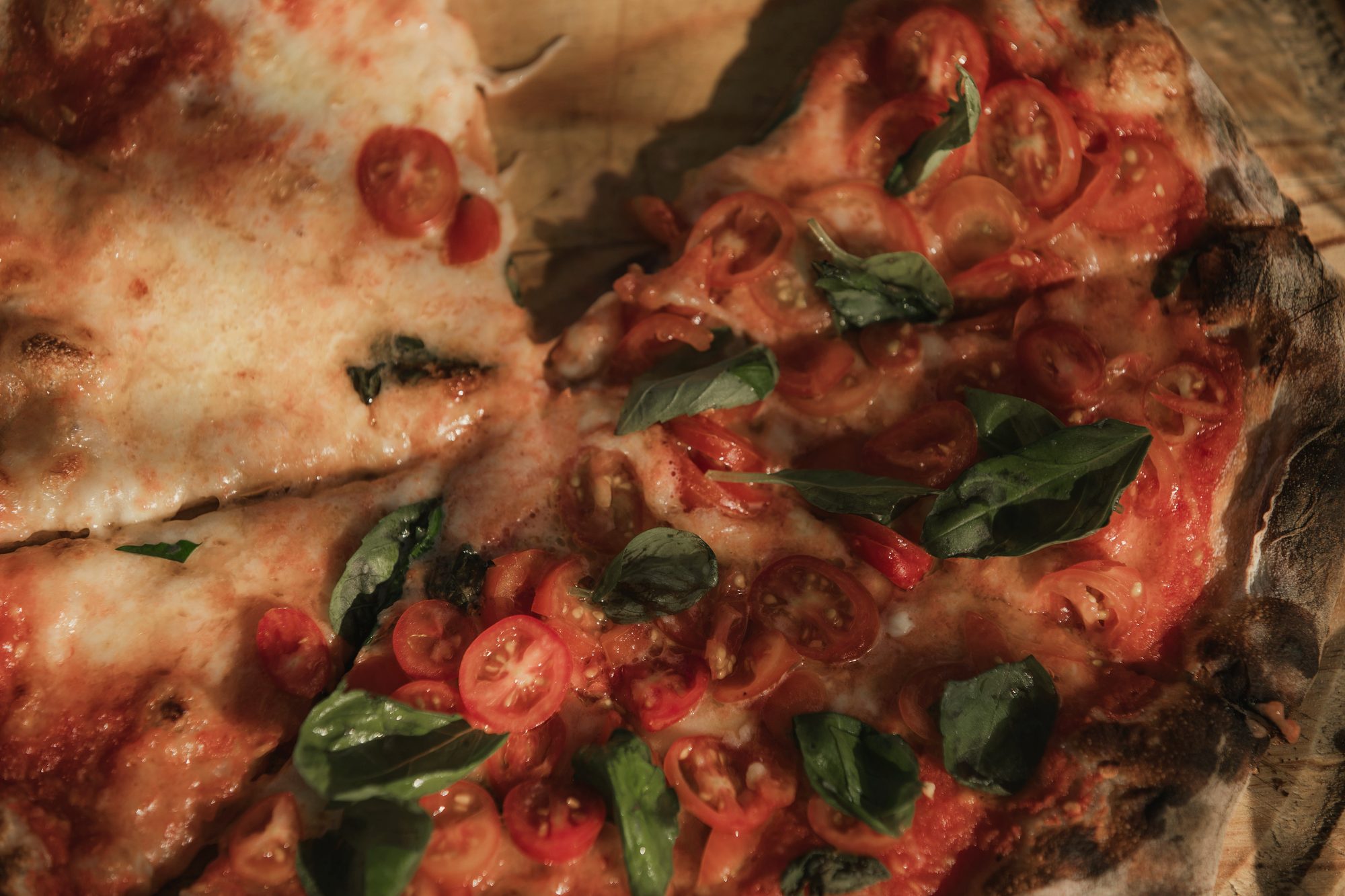 A charred margherita with basil and blistered tomato, plated on wood at the oak table