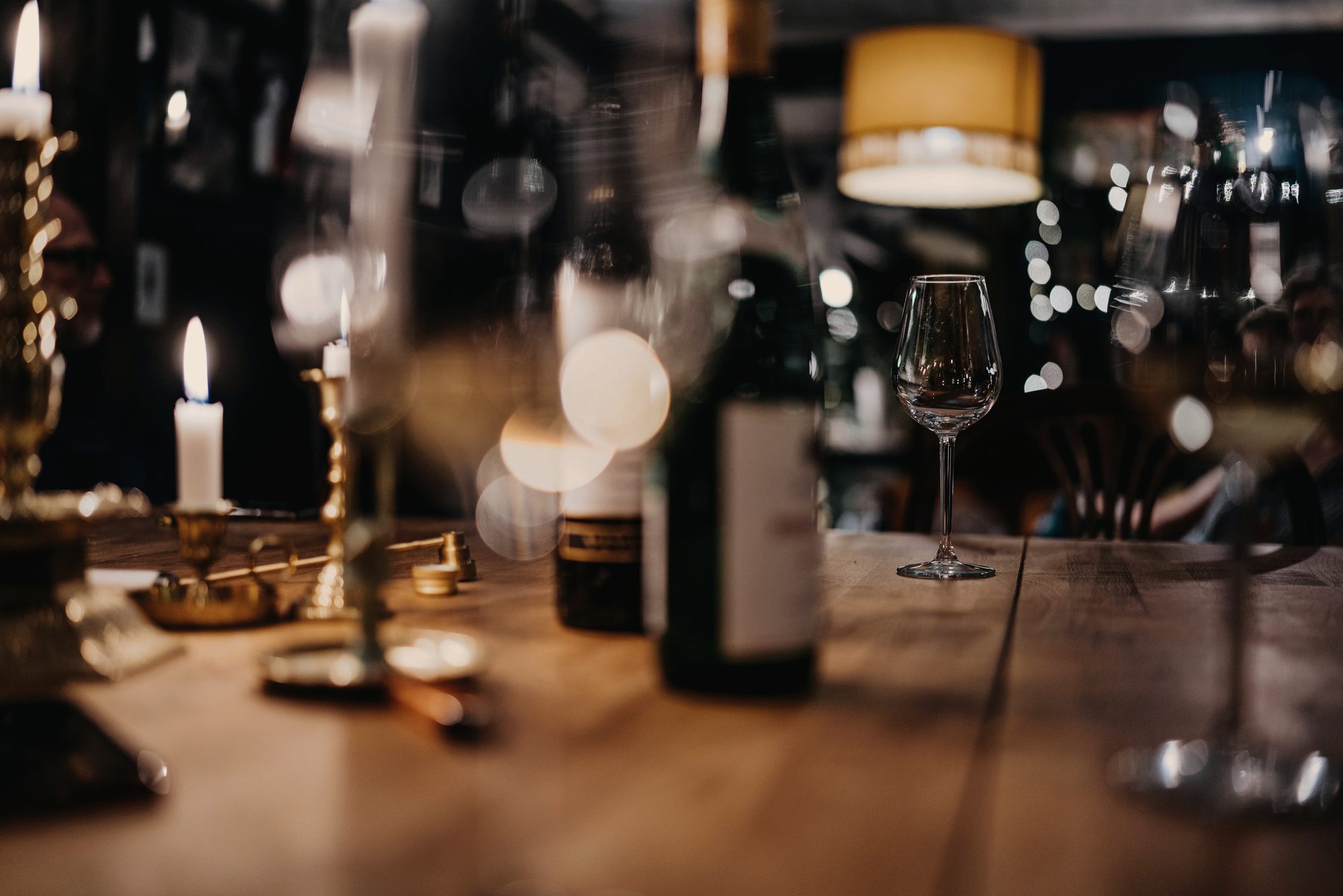 Candlelight, an open bottle and a glass on the bar at Ember and Oak